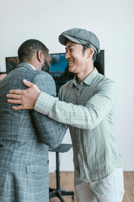 Two men in professional attire greet each other with a handshake and smiles.