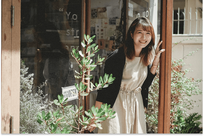 A young woman smiles and poses with a peace sign in front of a shop.