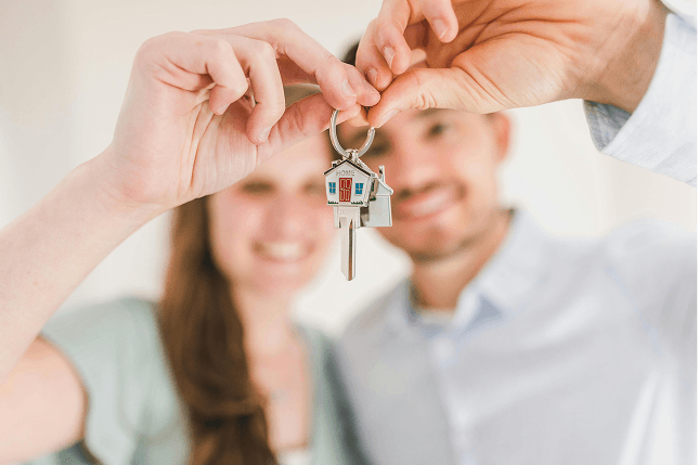A couple holds up a set of house keys with a house-shaped keychain.